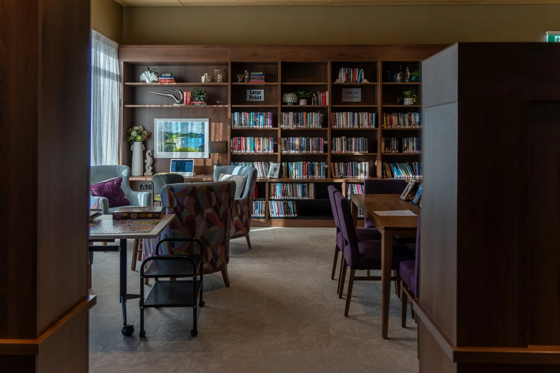 The library, with full-height bookshelves, a large-print section and armchairs set around a games table