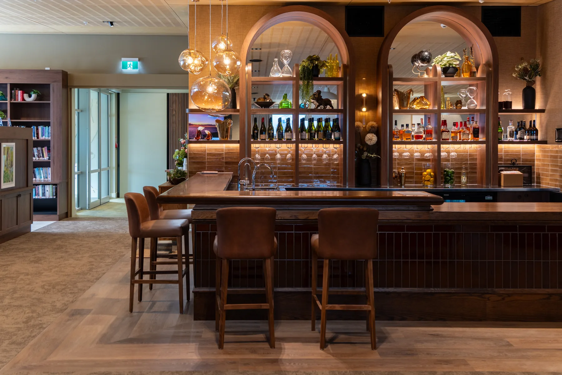 The bar, with leather stools along the counter and arched shelving lit behind it