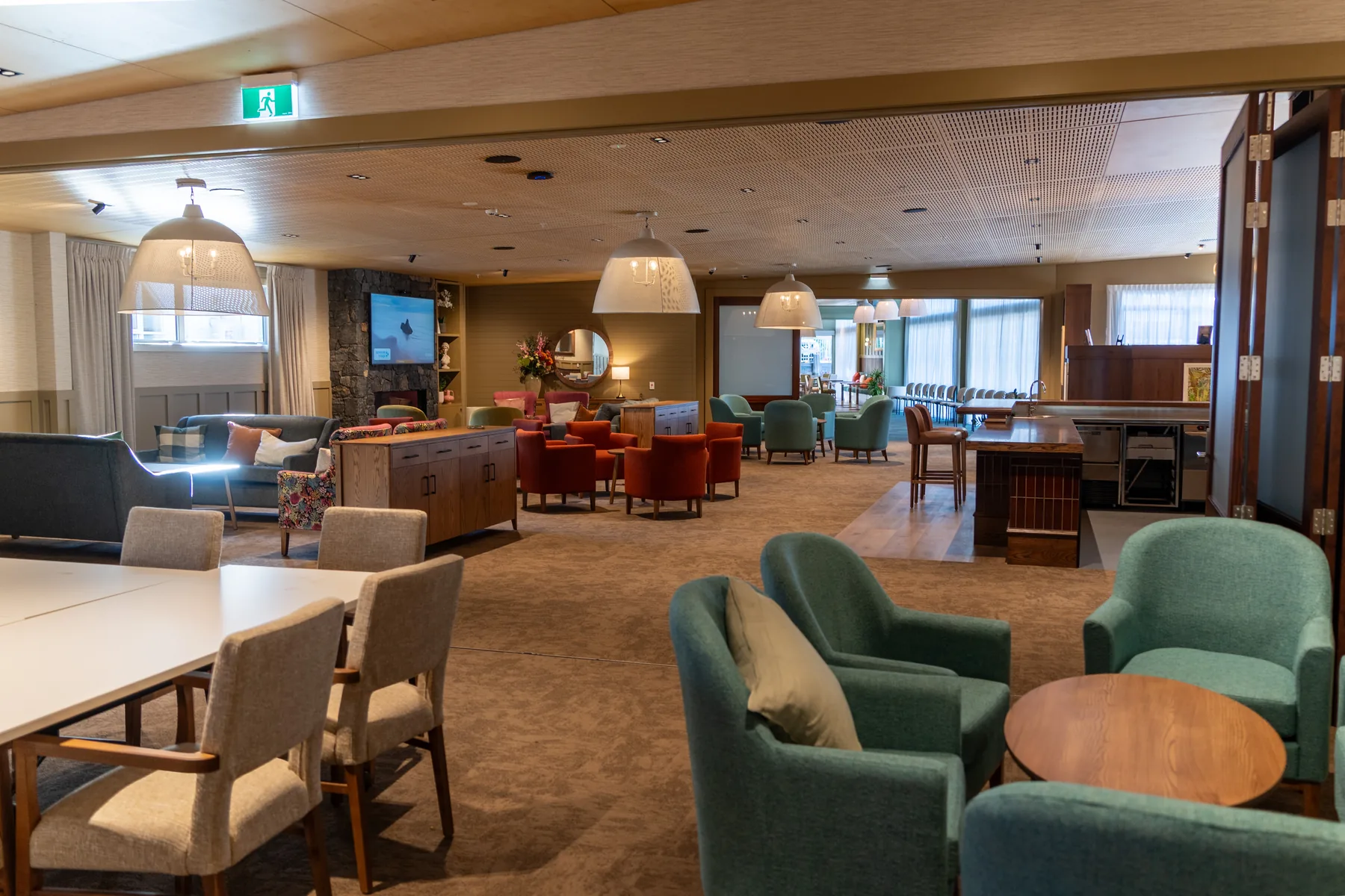 The main community centre lounge, with armchairs and dining tables arranged in groups beneath pendant lights