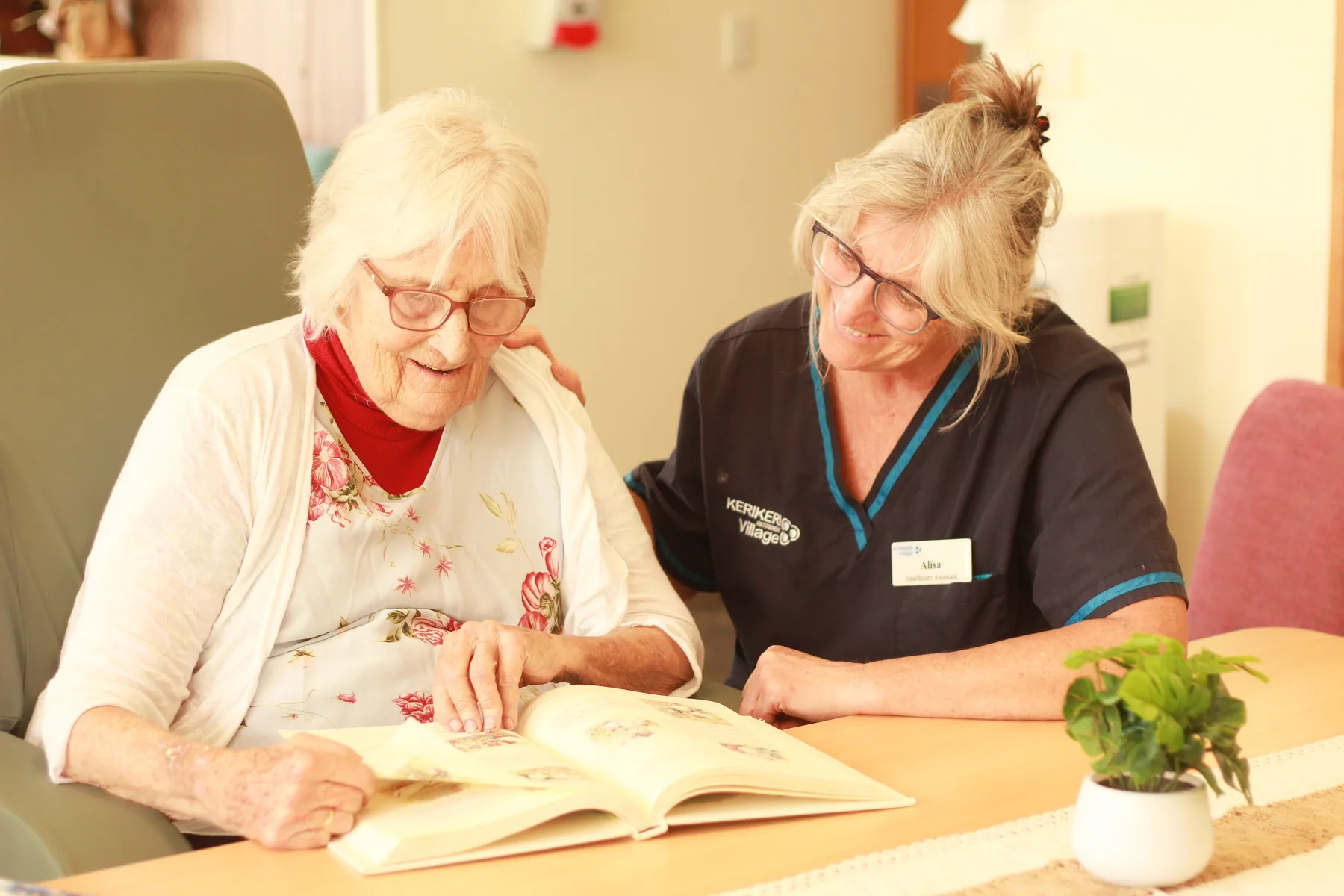 A nurse in village uniform sitting alongside a resident, looking through a book together
