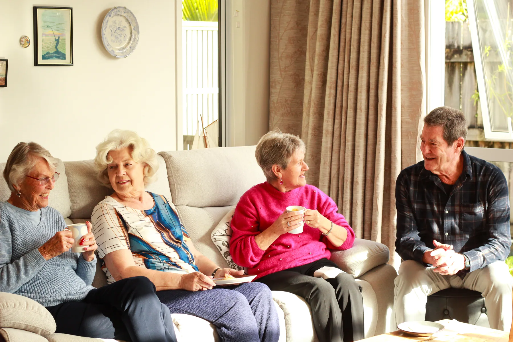 Four residents sitting together with cups of tea, talking and laughing in a village lounge