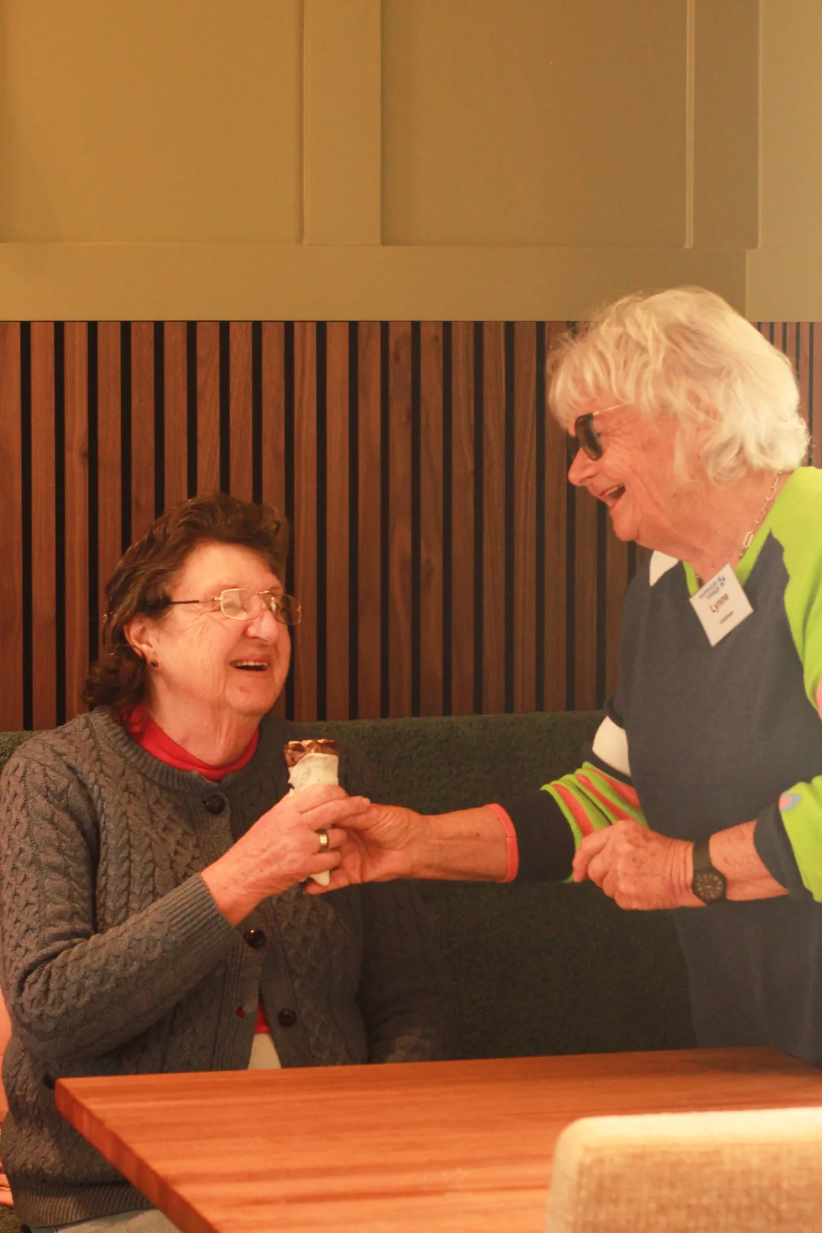 A staff member handing a resident a warm drink in the care centre lounge