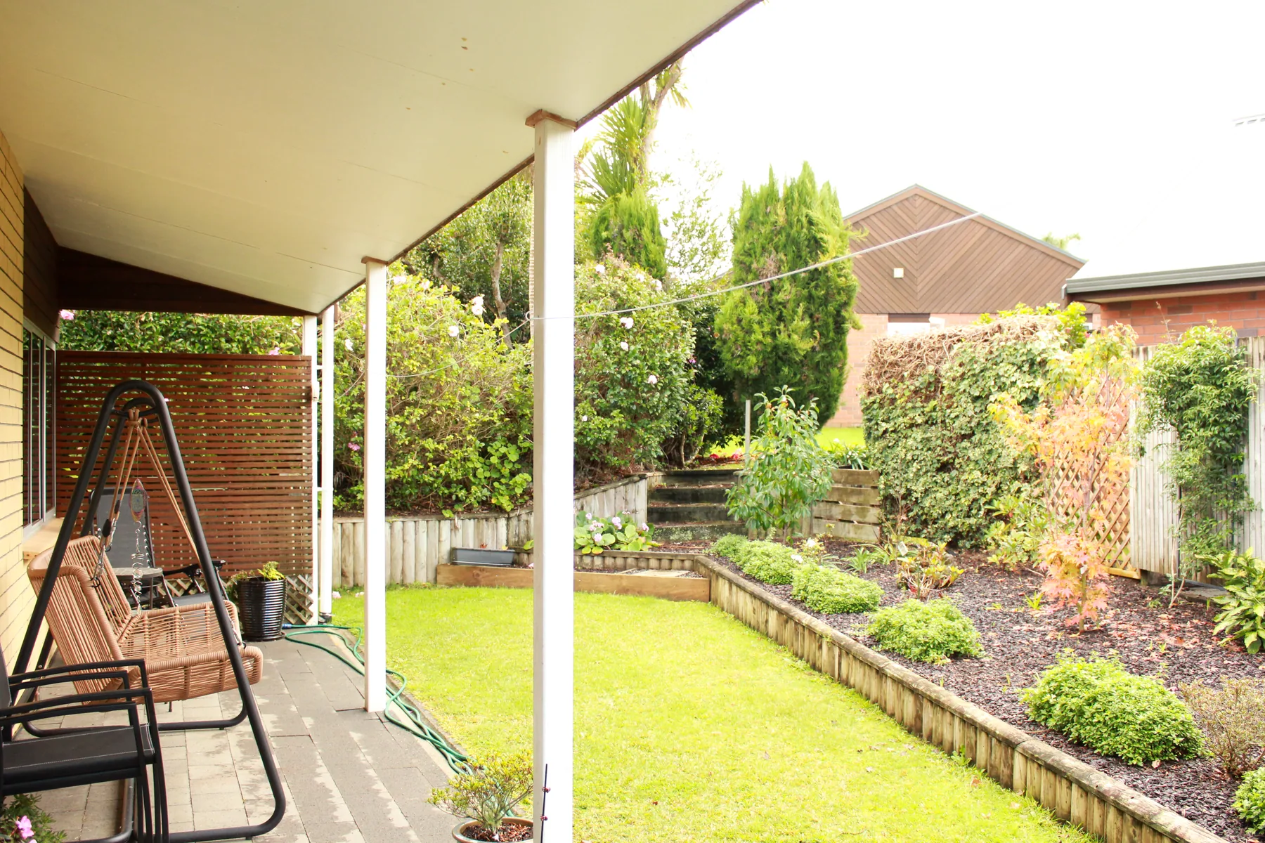 A covered cottage patio with a swing seat, looking down a planted garden