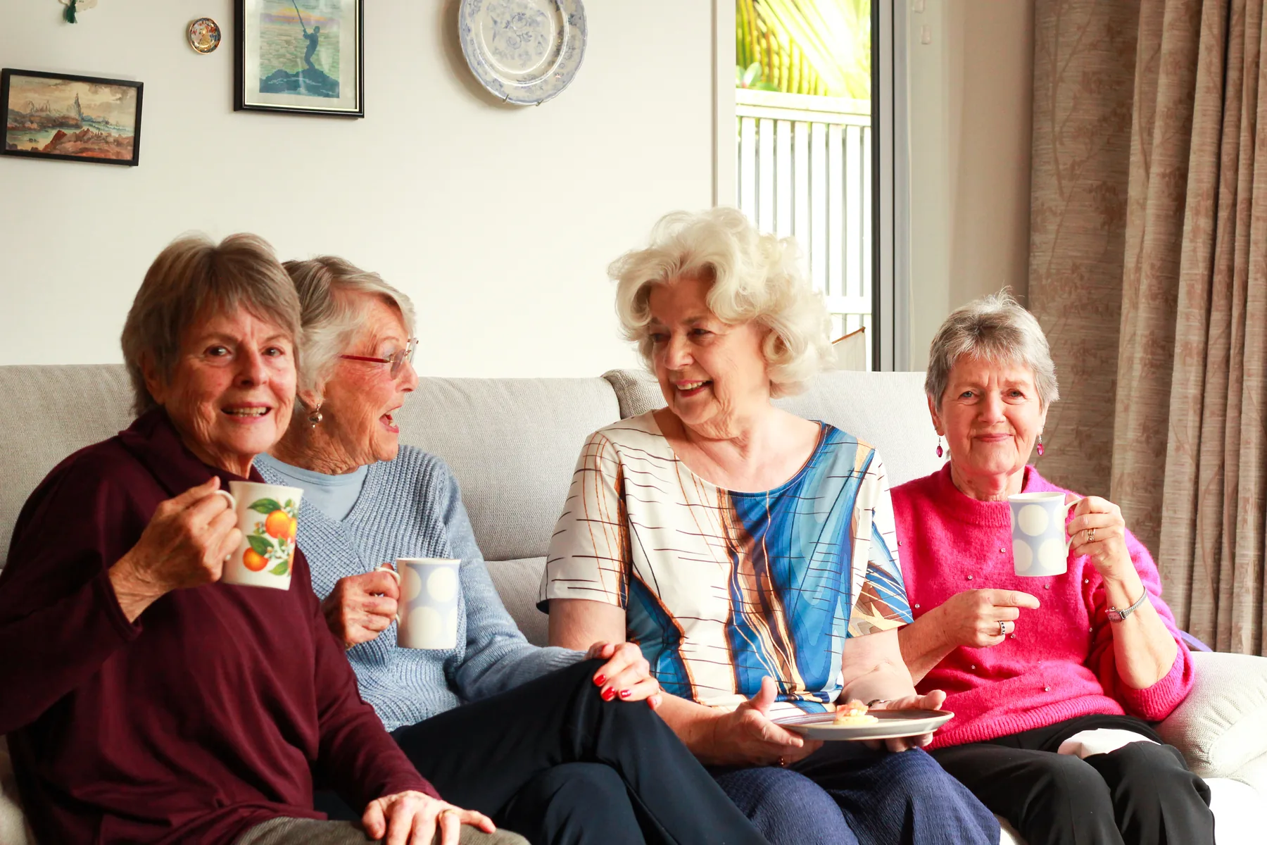 Four friends laughing together over a cup of tea