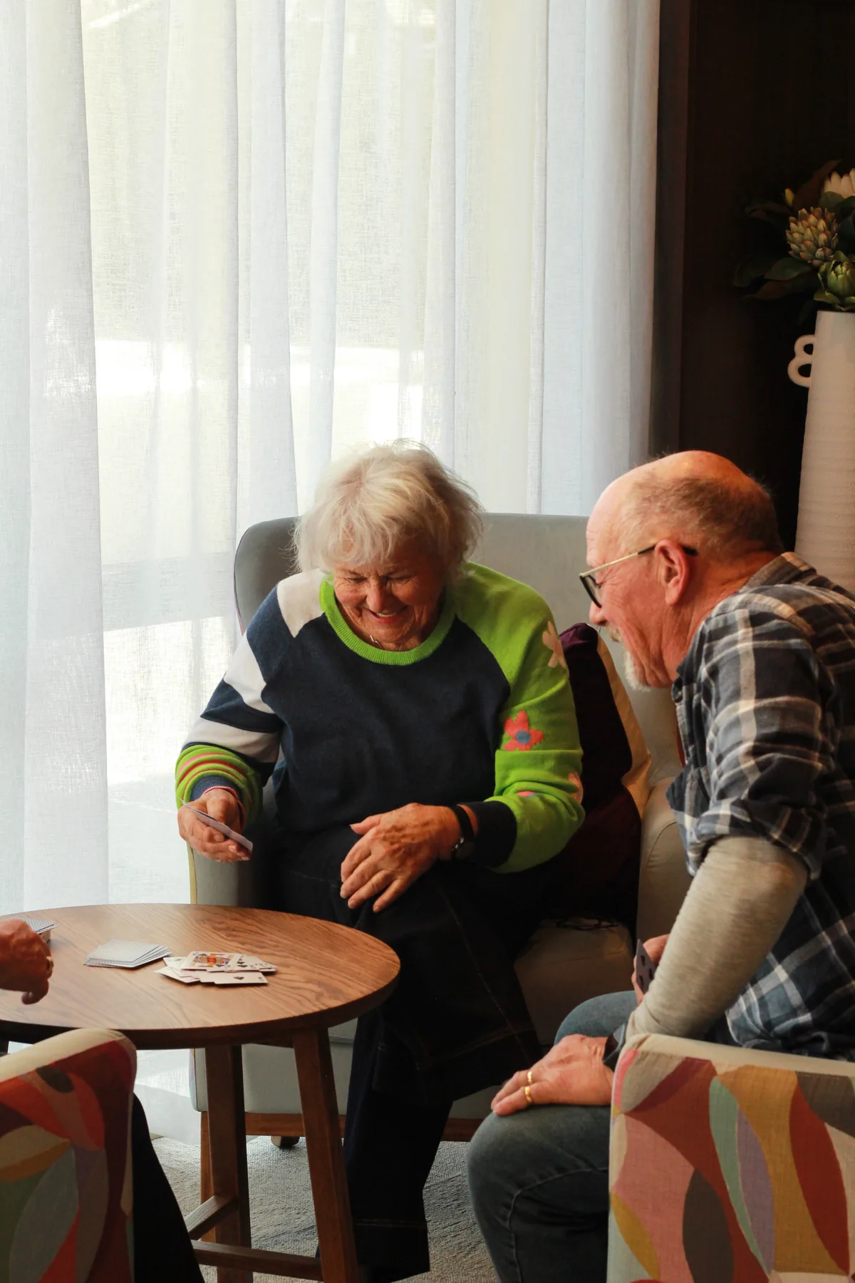 A volunteer and a resident playing cards together by a sunny window